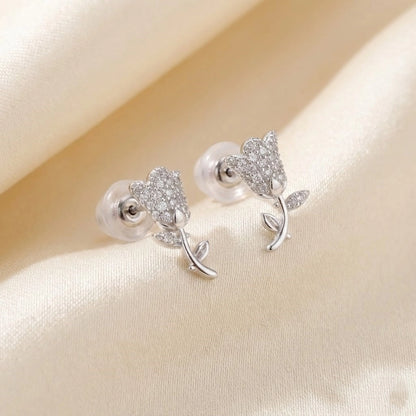 Silver rose-shaped earrings on a beige fabric background