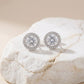 Silver earrings with clear gemstones on a textured beige surface