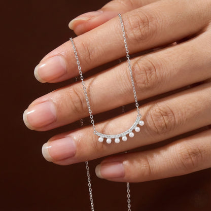 Silver necklace with a small pendant held by a hand against a dark background