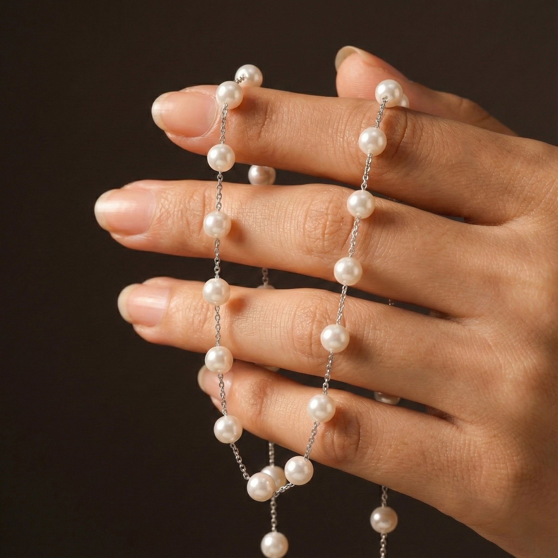 Pearl necklace draped over a hand against a dark background