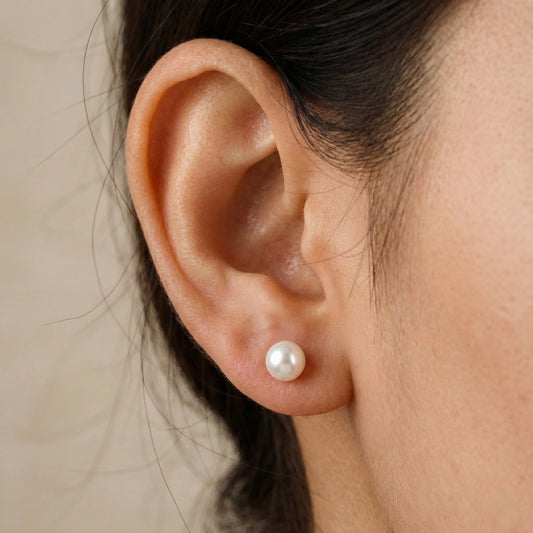 Close-up of an ear wearing a pearl earring with a neutral background