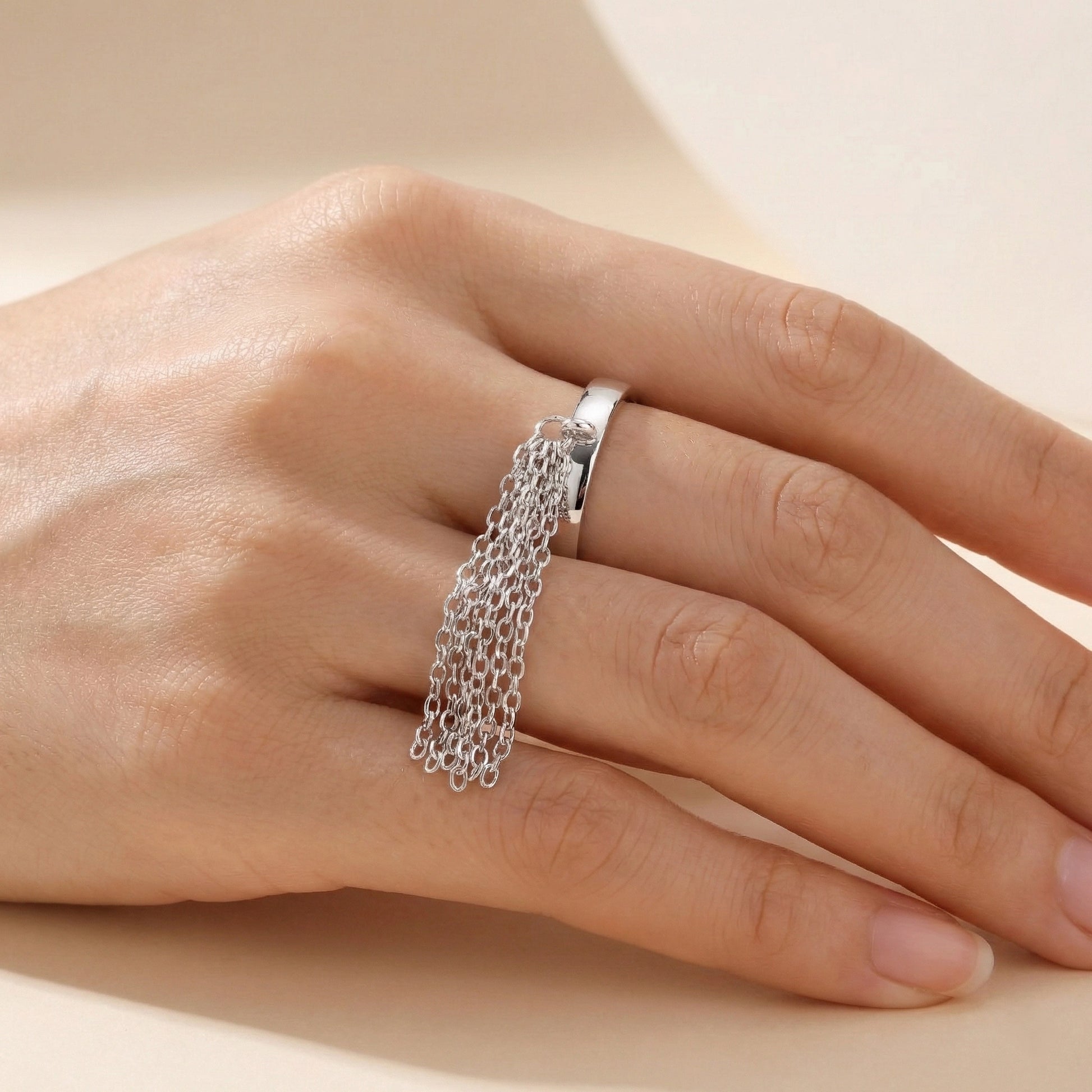 Silver chain ring on a person's finger against a neutral background