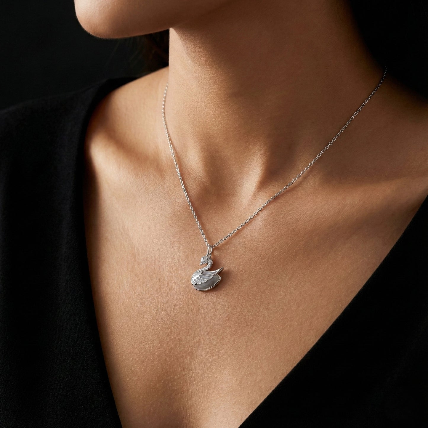 Silver necklace with a pendant on a person wearing a black outfit against a dark background