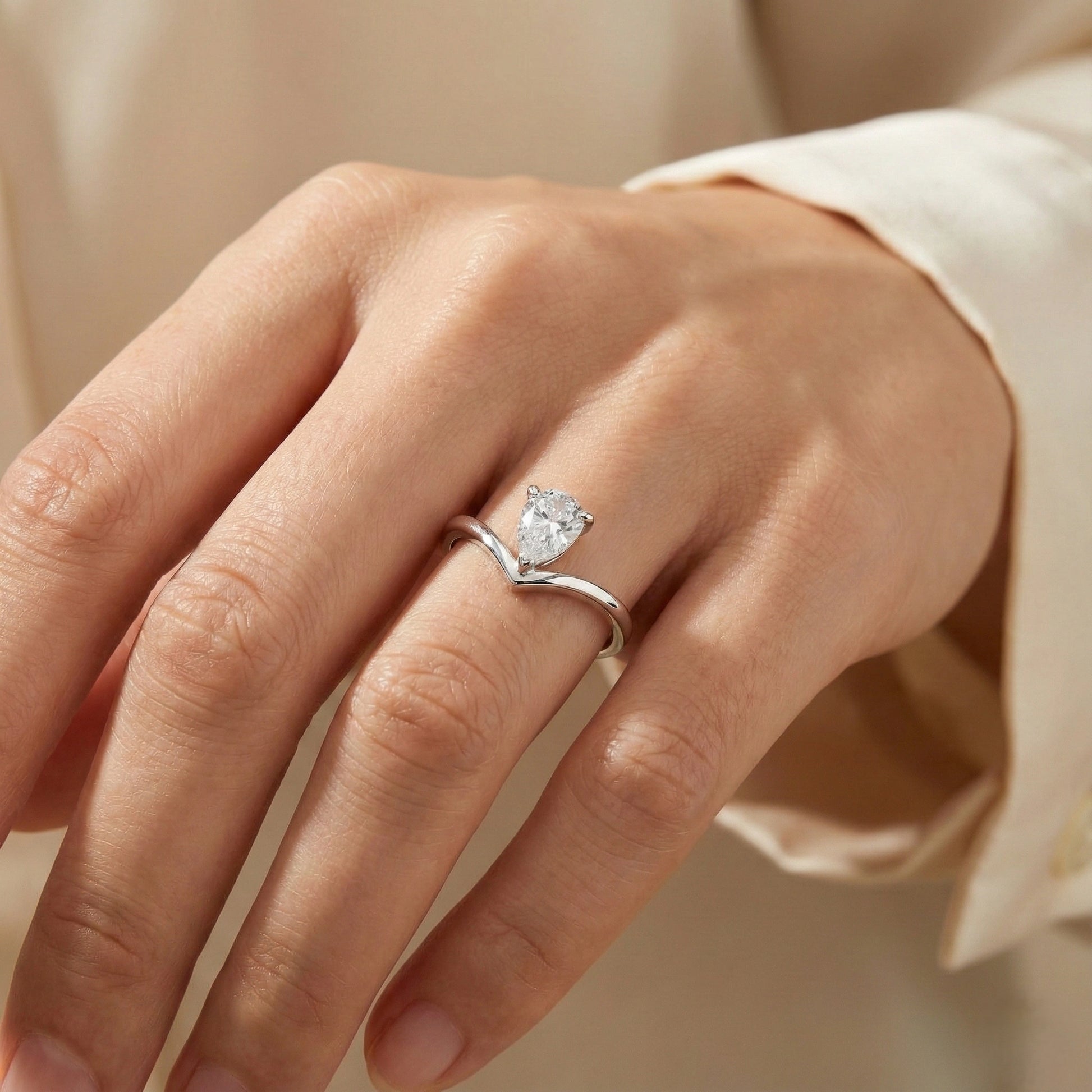Silver ring with a diamond on a person's finger against a neutral background