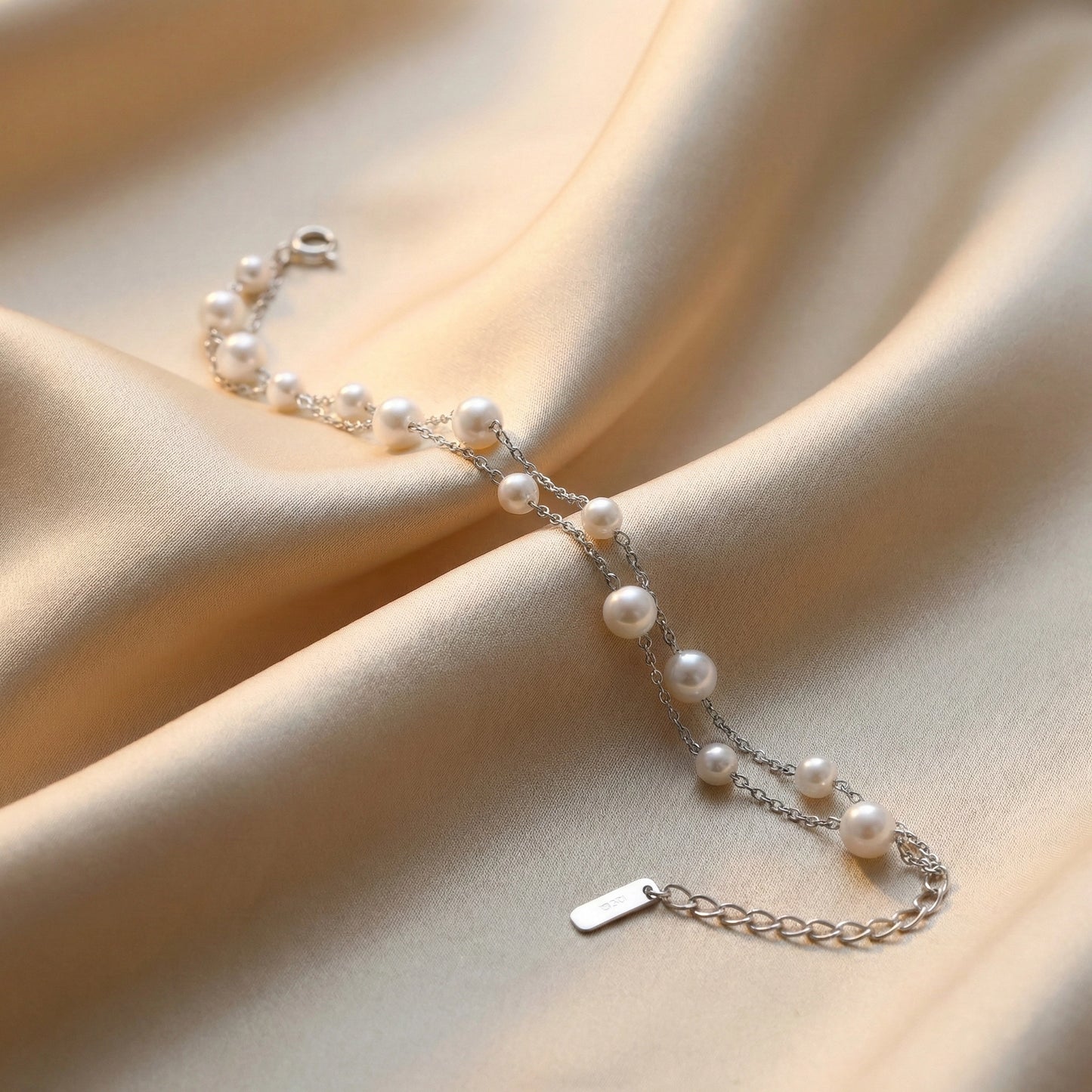 Silver chain bracelet with white pearls placed on beige satin fabric