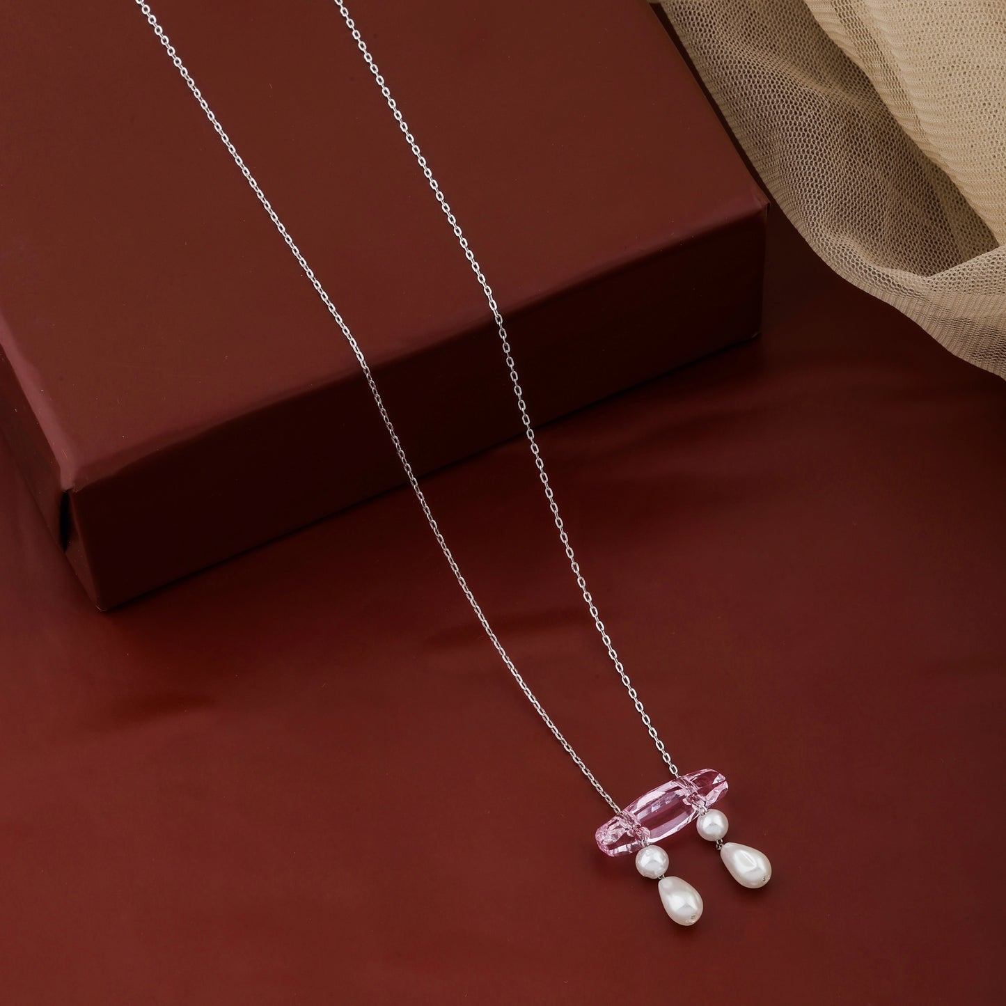 Necklace with a pink pendant and white beads on a red surface