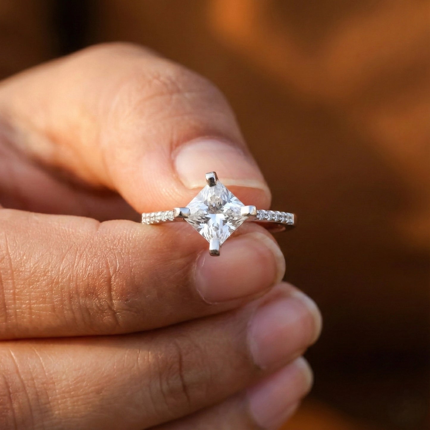 Diamond ring held between two hands against a neutral background