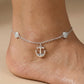 Silver anklet with an anchor charm on a foot against a beige background