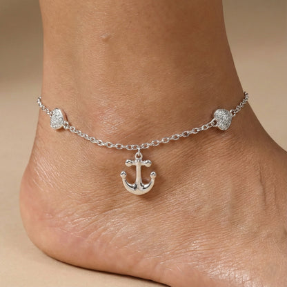 Silver anklet with an anchor charm on a foot against a beige background