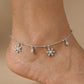 Silver anklet with snowflake charms on a person's ankle against a beige background