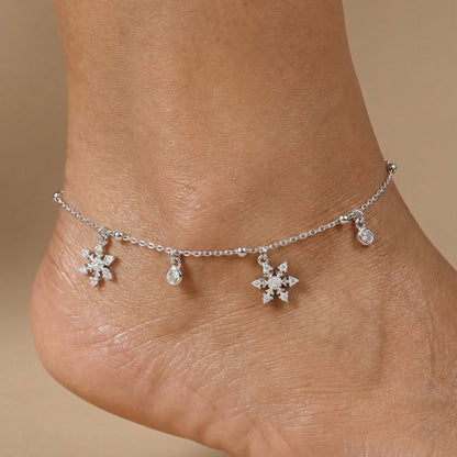 Silver anklet with snowflake charms on a person's ankle against a beige background