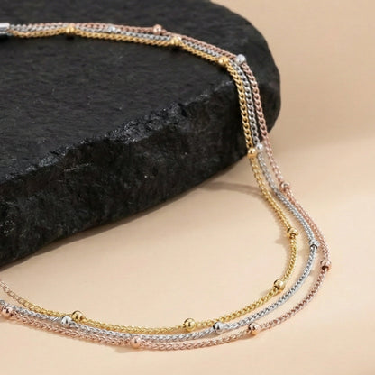Multistrand necklace with gold, silver, and rose gold tones on a dark stone surface.