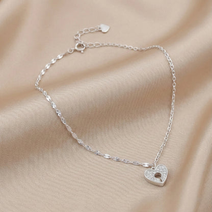 Silver bracelet with a heart-shaped charm on a beige fabric background