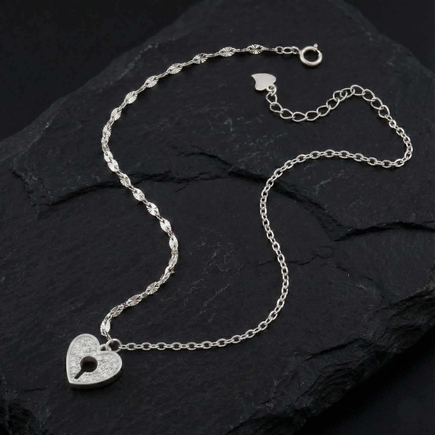 Silver necklace with a heart-shaped lock pendant on a dark stone surface
