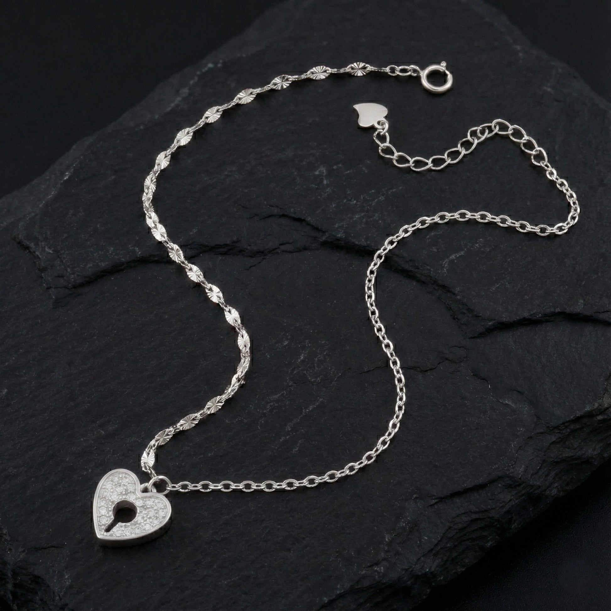 Silver necklace with a heart-shaped lock pendant on a dark stone surface