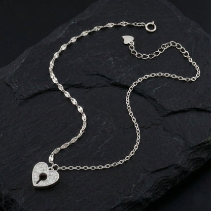 Silver necklace with a heart-shaped lock pendant on a dark stone surface