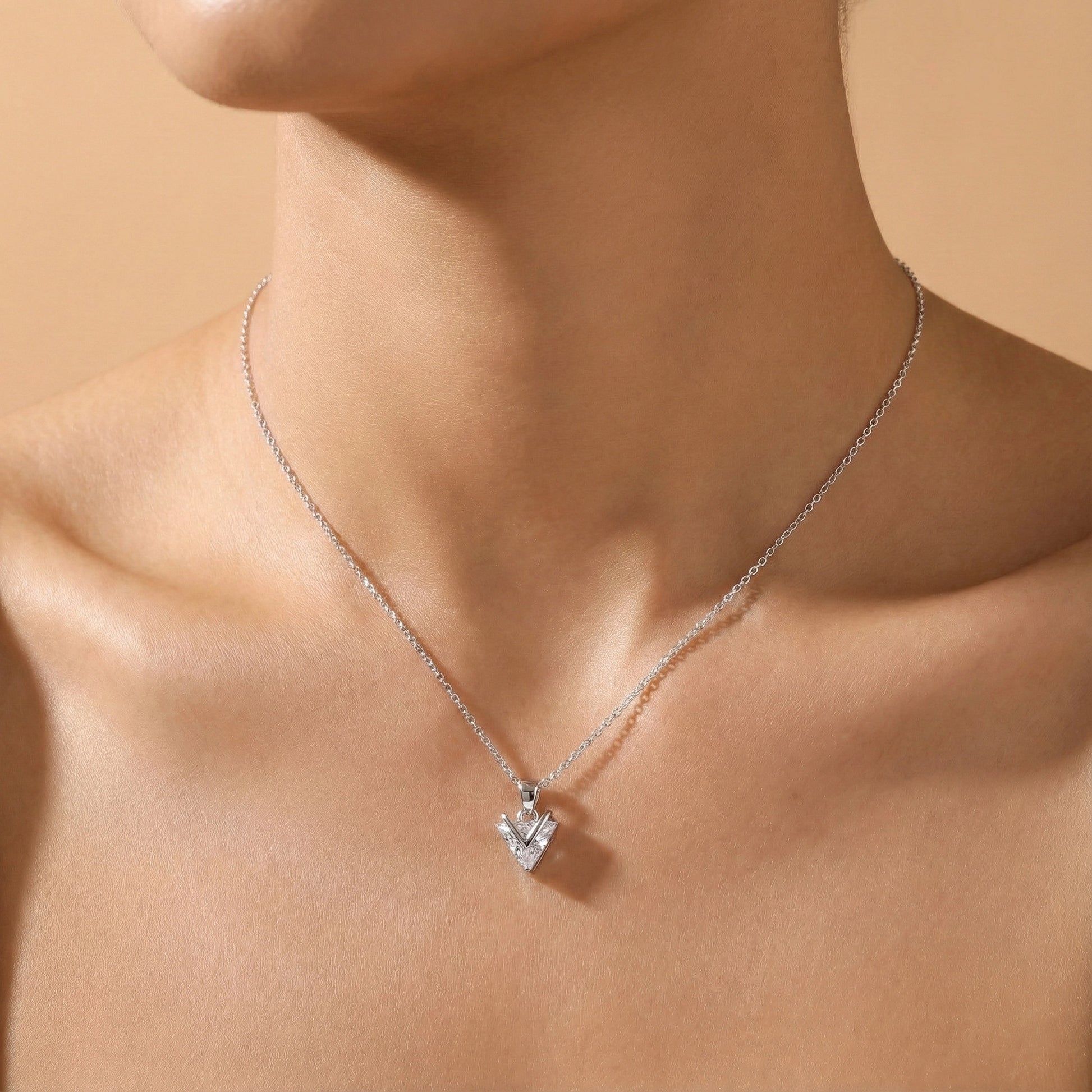Silver necklace with a pendant on a person's neck against a beige background
