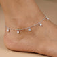 Silver anklet with small pendants on a person's ankle against a beige background