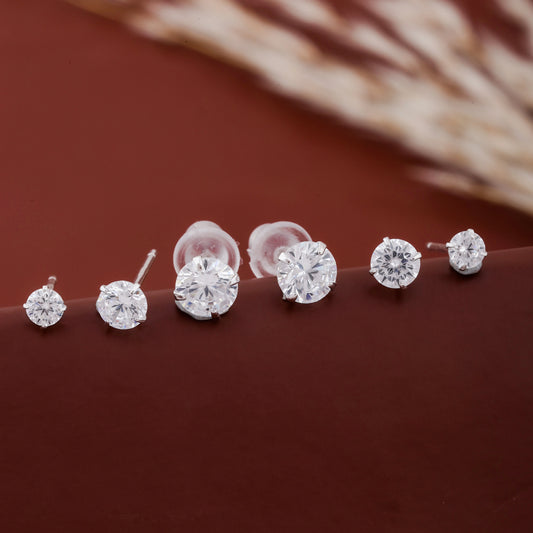 Close-up of silver solitaire stud earrings with sparkling round-cut stones on brown background