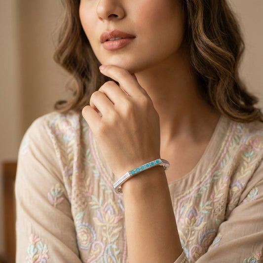 Woman wearing a silver bracelet with a blue gemstone, against a neutral background