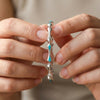 Silver bracelet with turquoise stones held between two hands against a neutral background