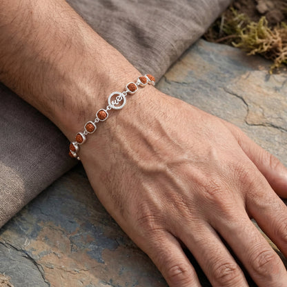 Hand wearing a silver bracelet with orange stones on a stone surface
