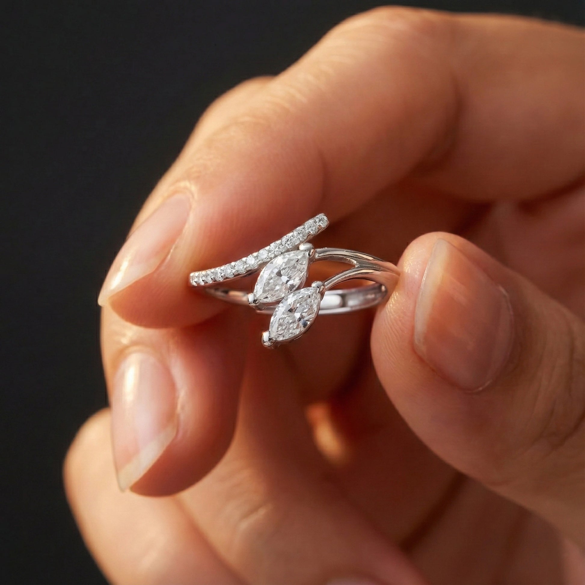 Silver ring with diamonds held between fingers against a dark background