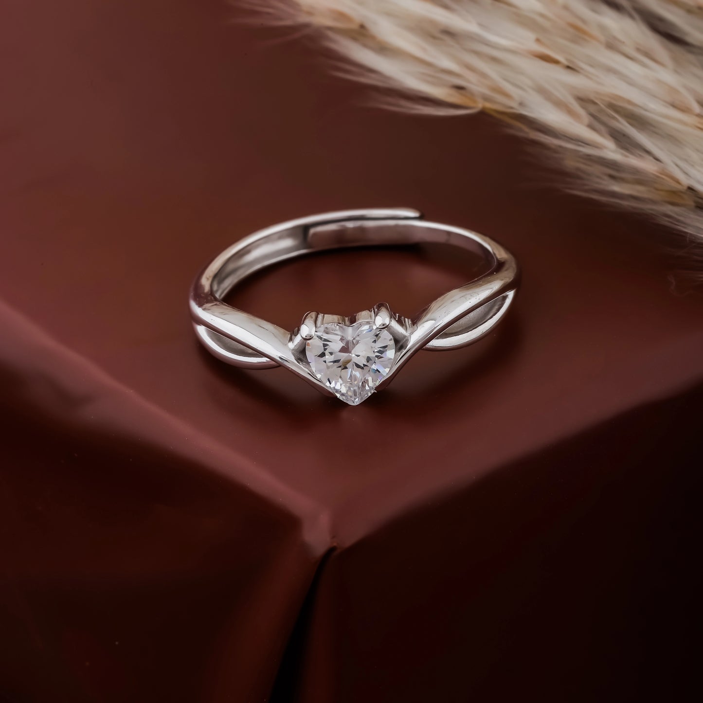 Silver ring with a heart-shaped diamond on a brown fabric background