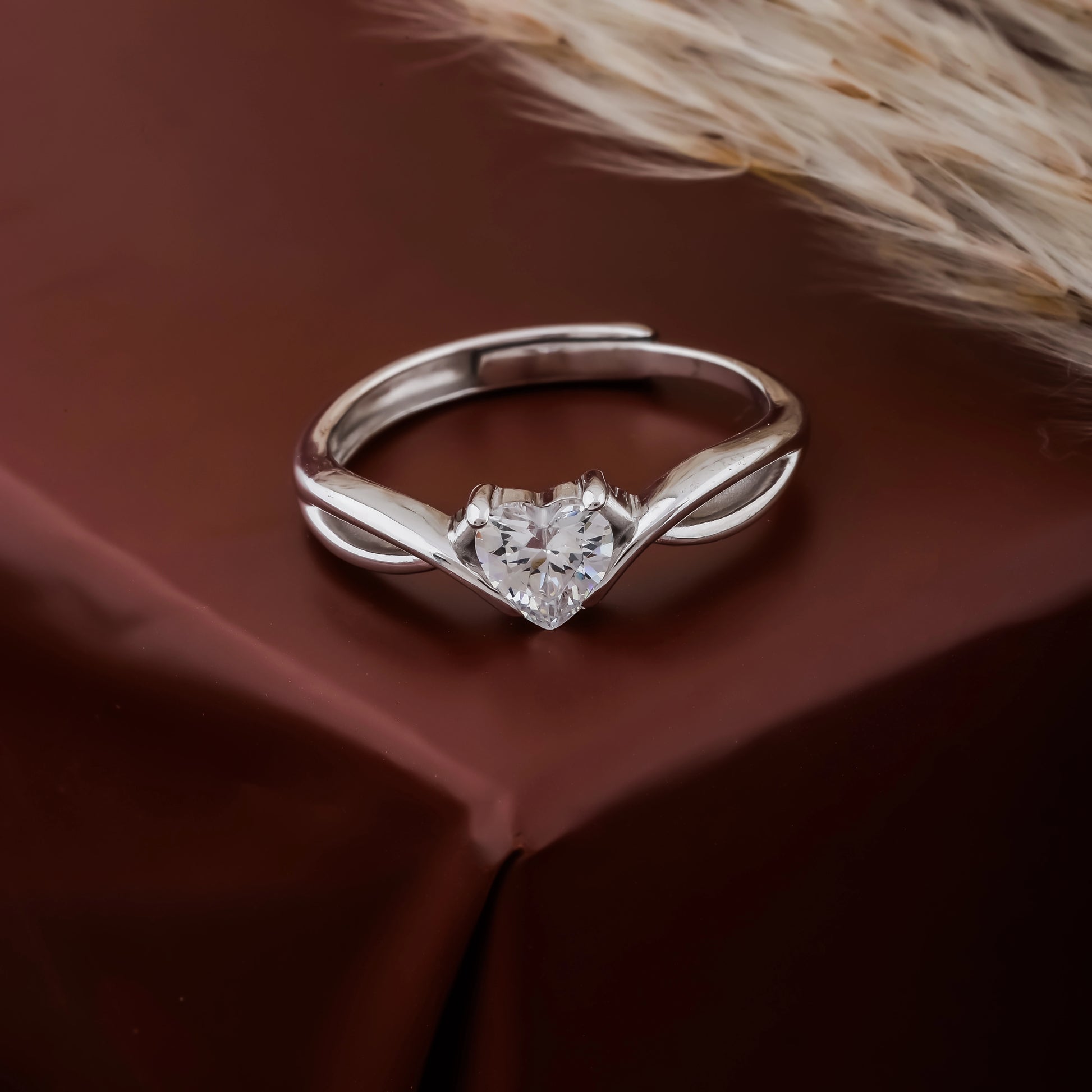 Silver ring with a heart-shaped diamond on a brown fabric background