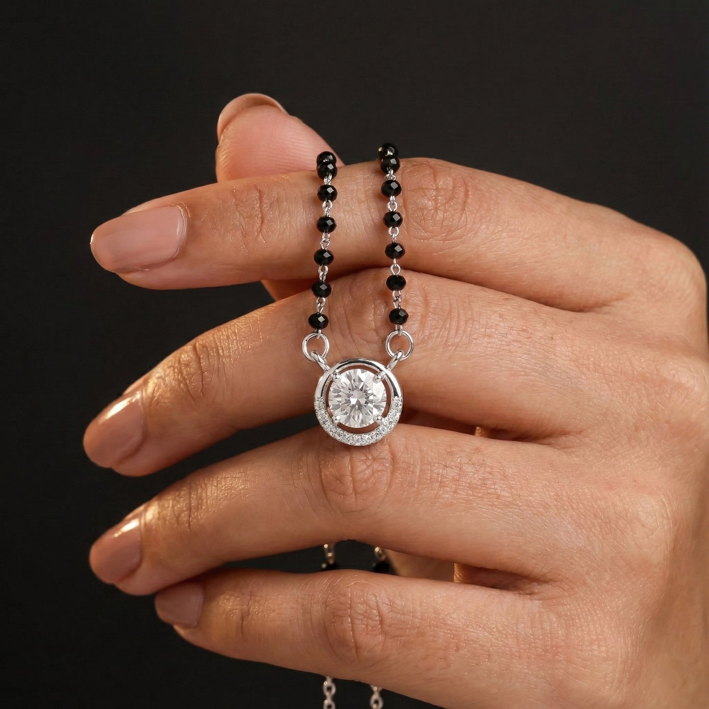 Hand holding a necklace with a diamond pendant against a dark background
