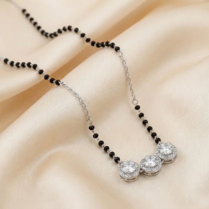 Necklace with black beads and silver pendants on a beige fabric background