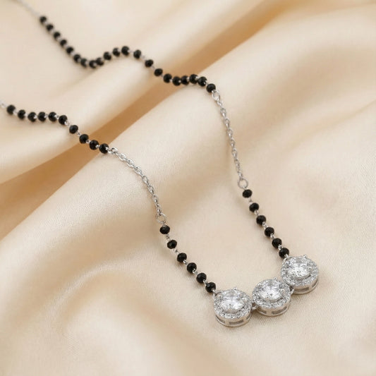 Necklace with black beads and silver pendants on a beige fabric background