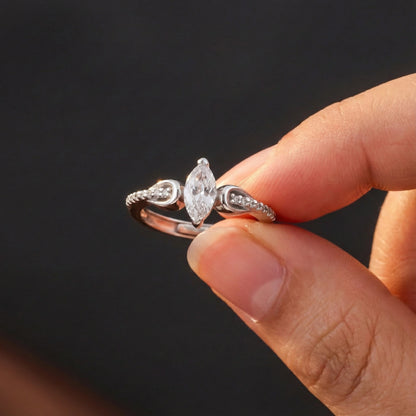 Silver ring with a diamond held between fingers against a dark background