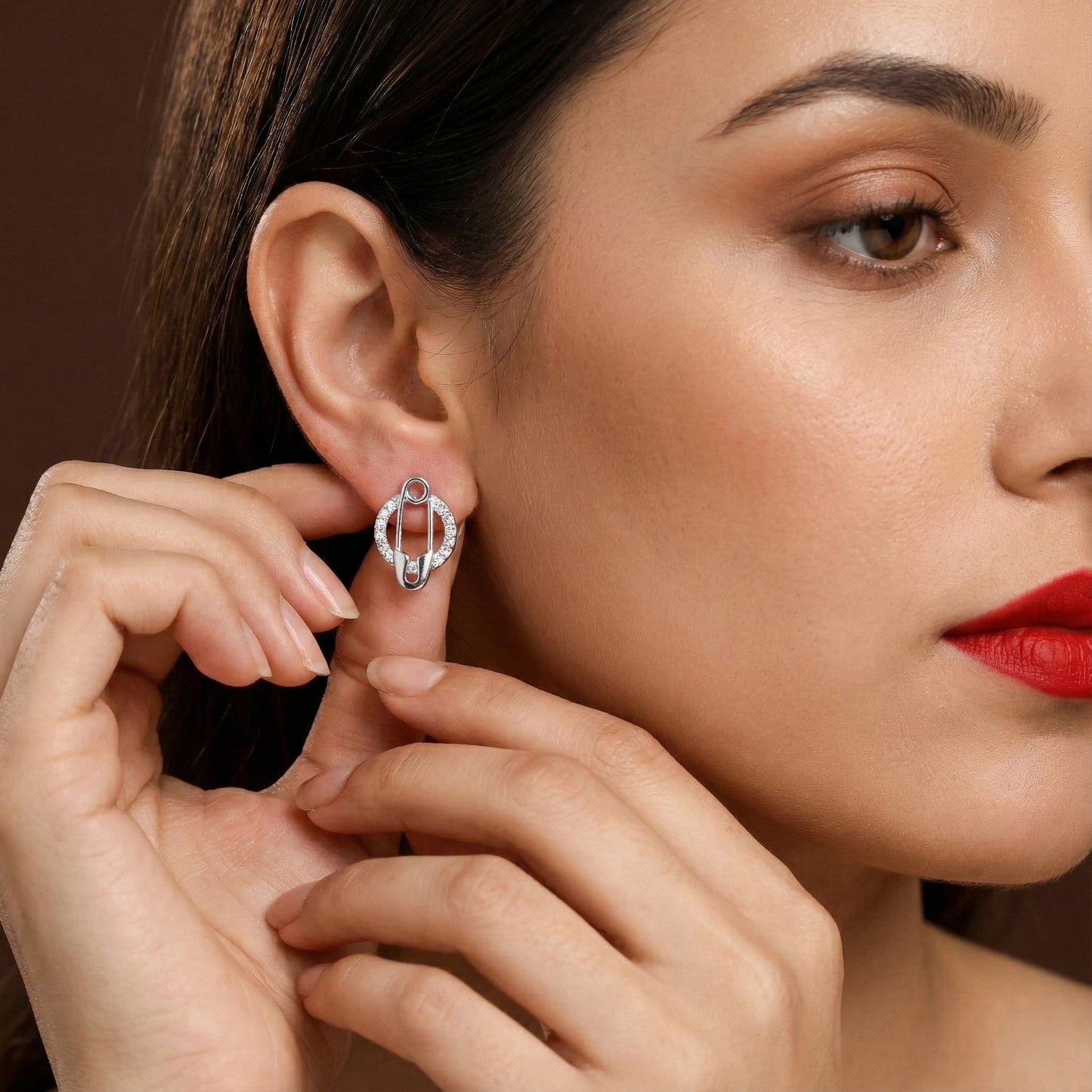 Close-up of a woman wearing a silver earring against a brown background