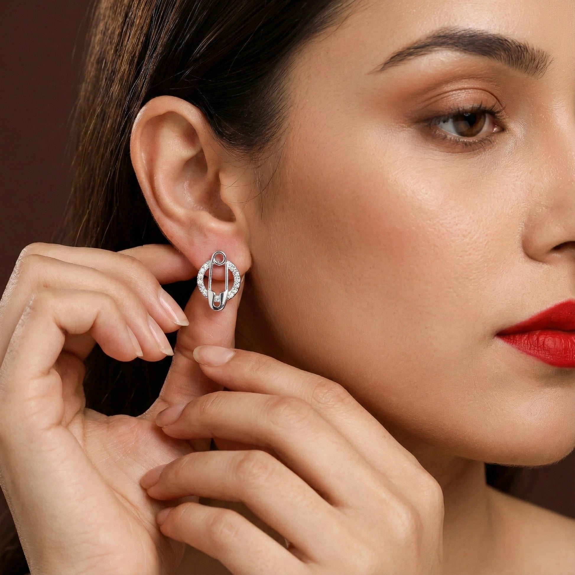 Close-up of a woman wearing a silver earring against a brown background