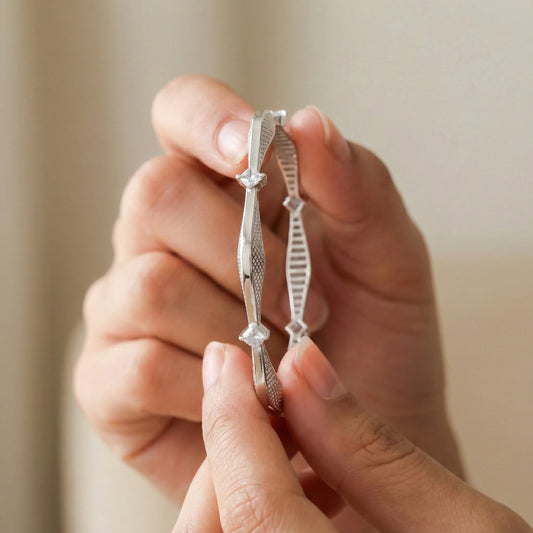 Two silver rings with intricate designs held between fingers against a neutral background
