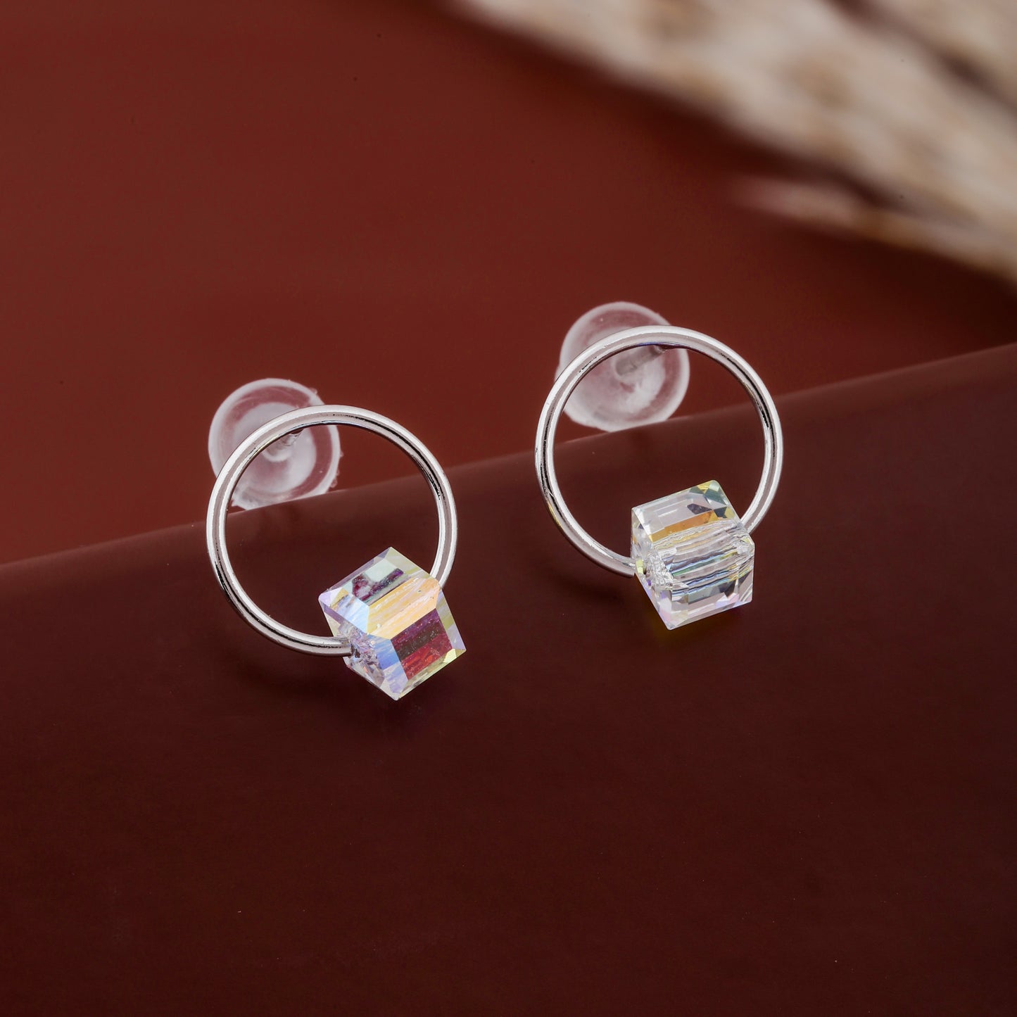 Silver hoop earrings with colorful square charms on a brown surface