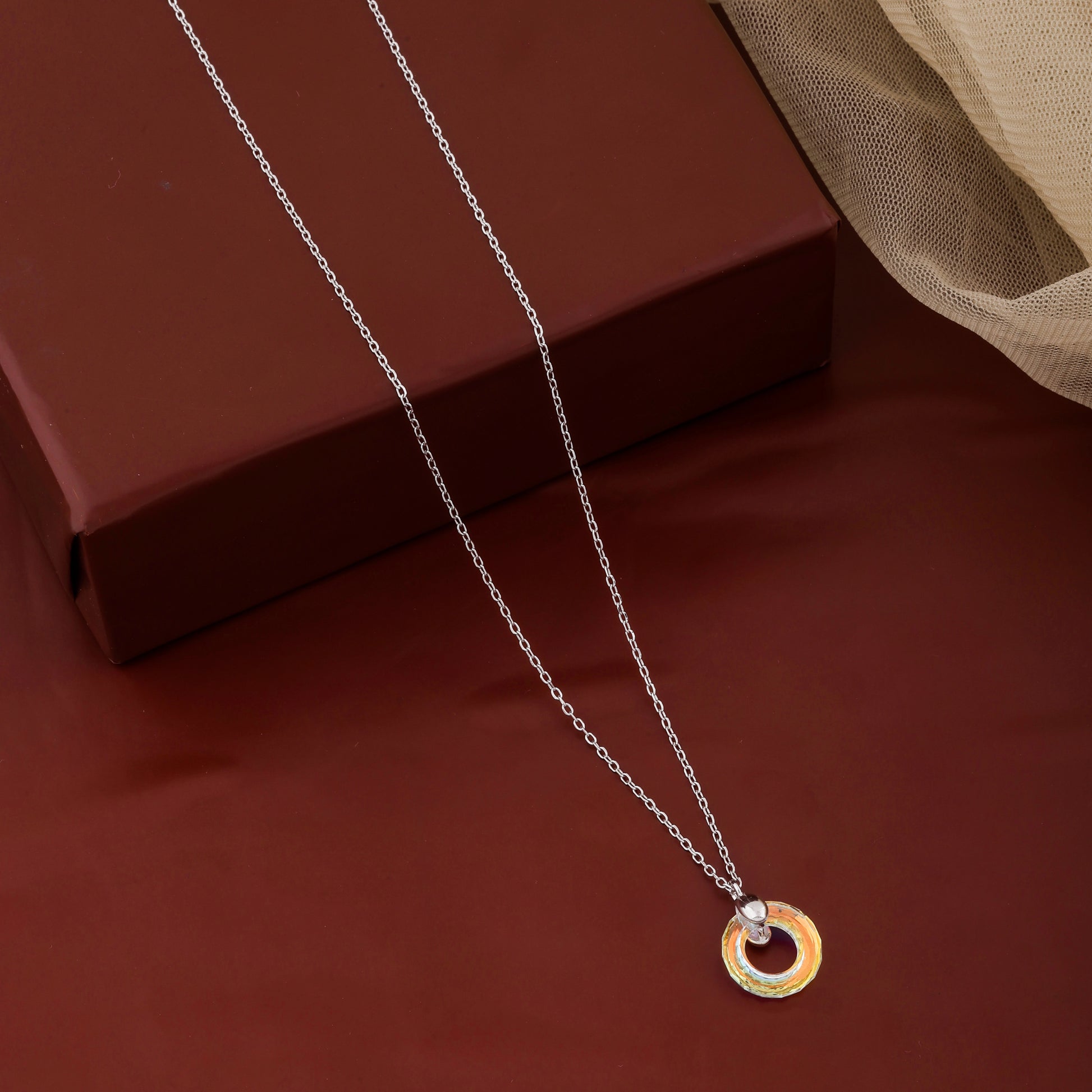 Necklace with a gold and silver pendant on a red surface