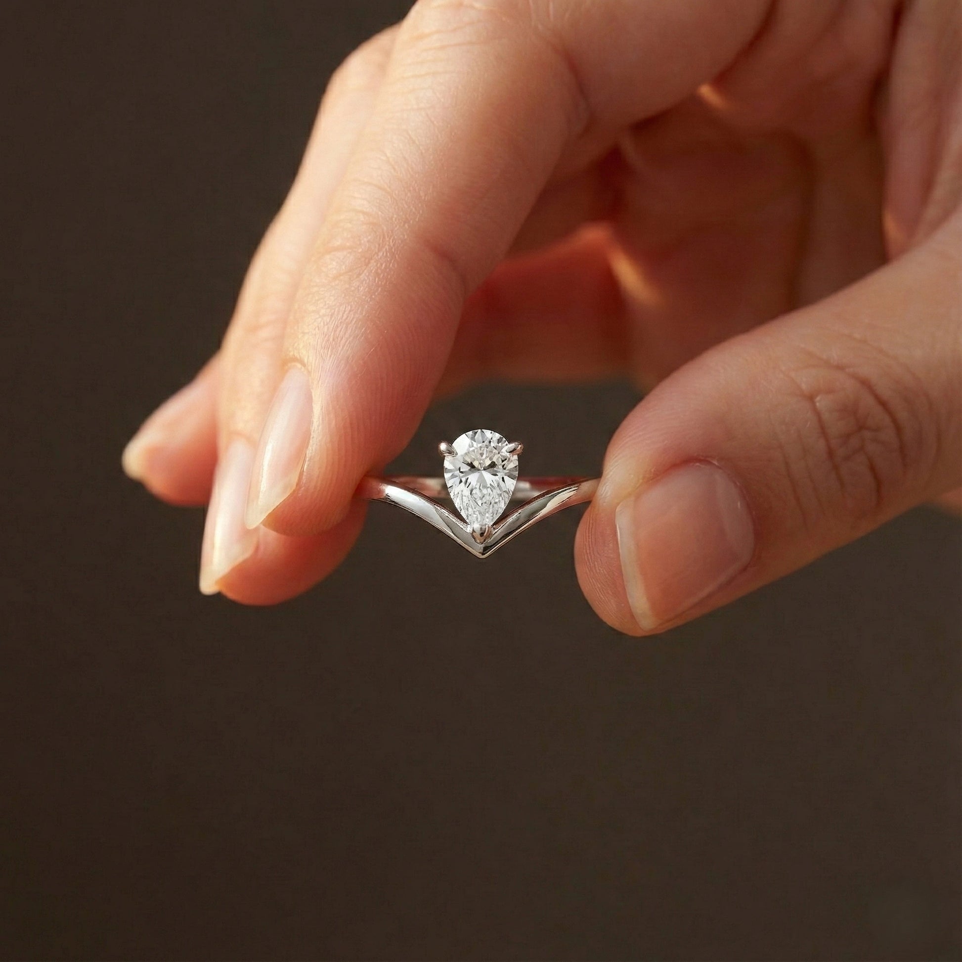 Close-up of a hand holding a diamond ring against a dark background