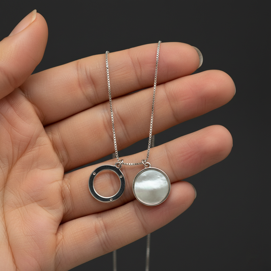 Hand holding a necklace with two pendants against a dark background