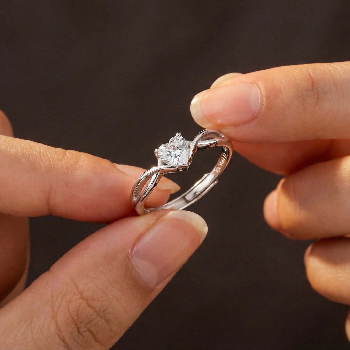 Silver diamond ring held between two fingers against a dark background
