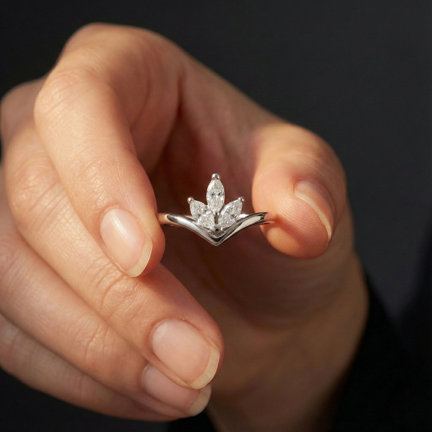 Hand holding a diamond ring with a dark background