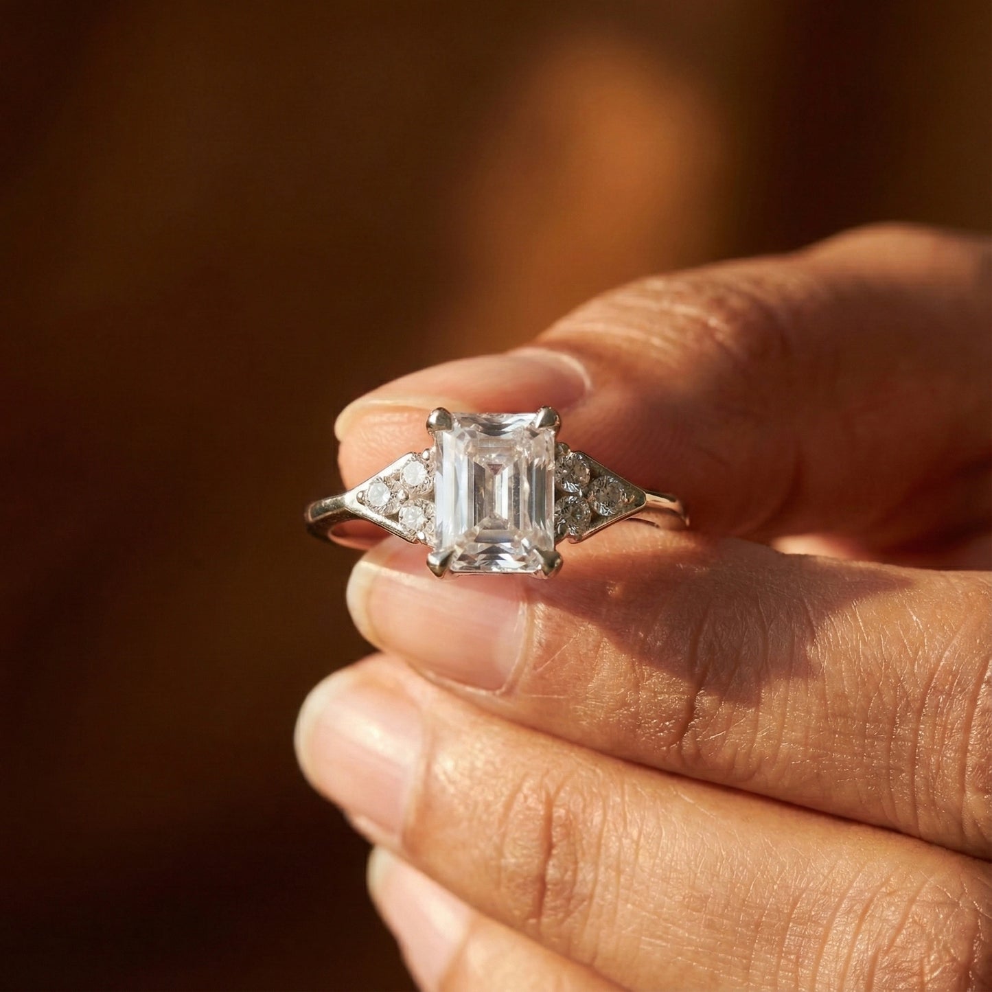 Diamond ring held in a hand with a warm, blurred background