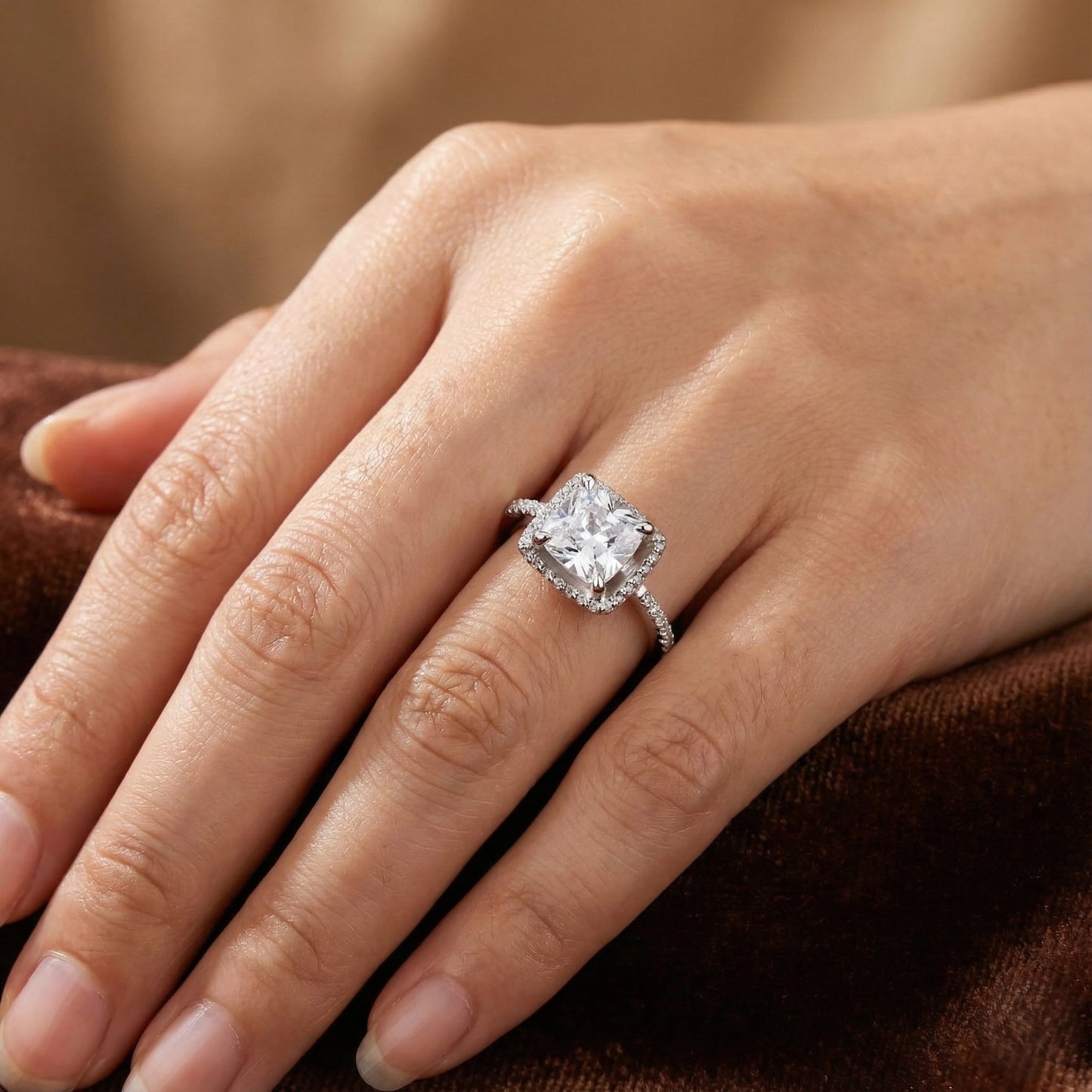 Close-up of a hand wearing a diamond ring on a brown fabric background