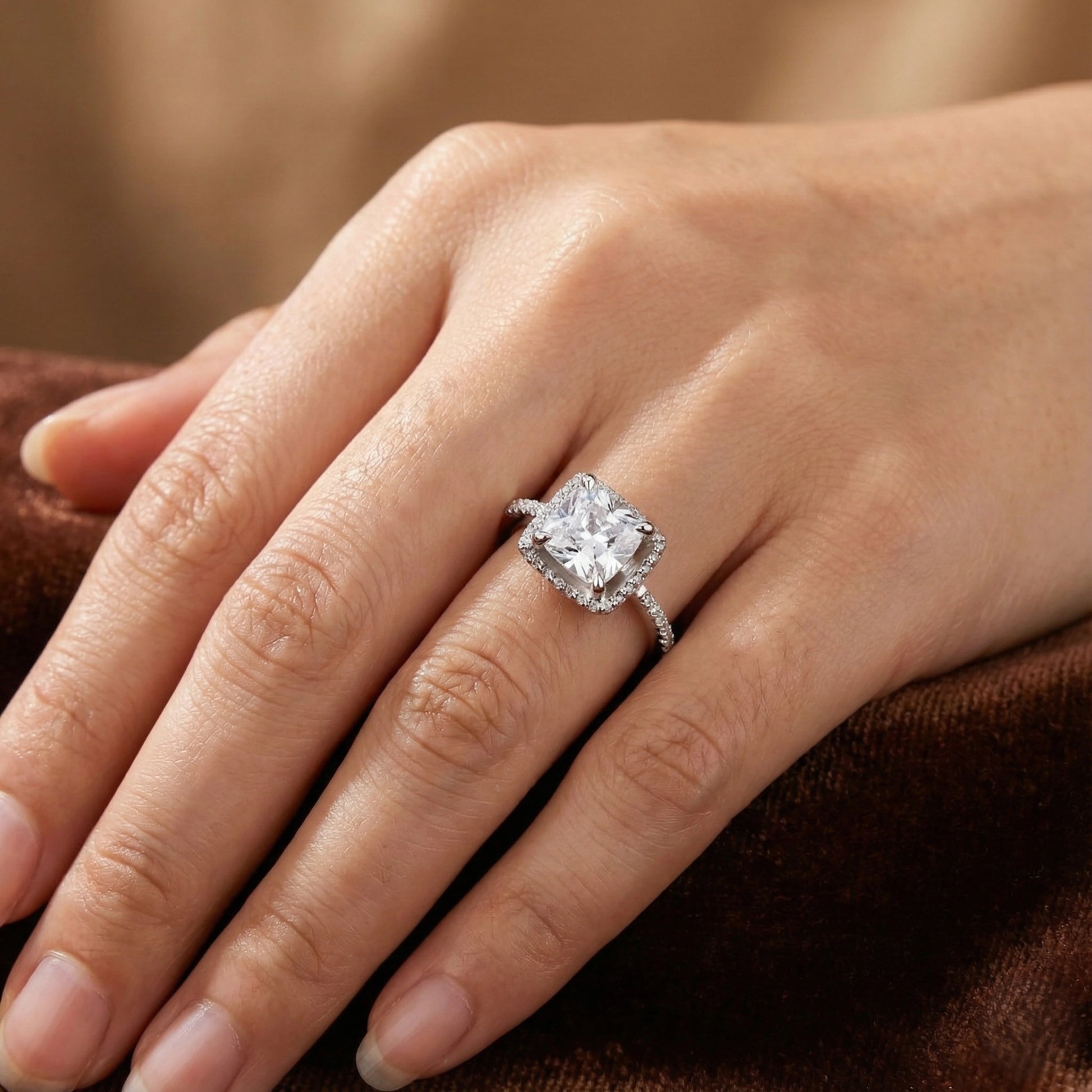 Close-up of a hand wearing a diamond ring on a brown fabric background