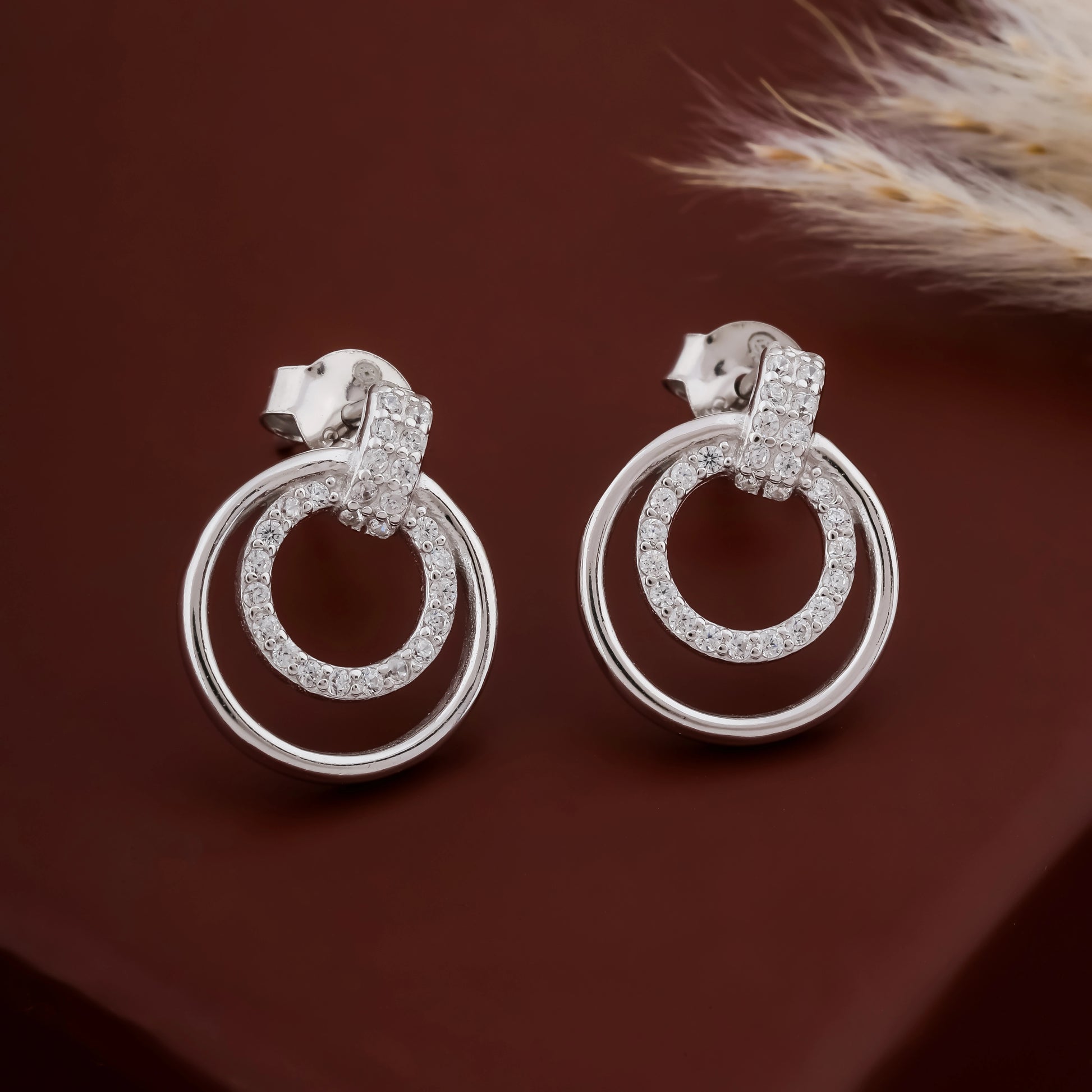 Silver hoop earrings with embedded diamonds on a dark brown background