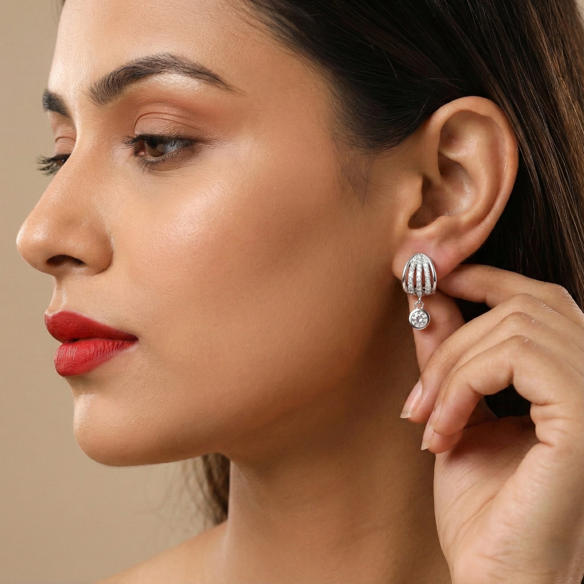 Close-up of a woman wearing a silver earring with a clear gemstone on a beige background