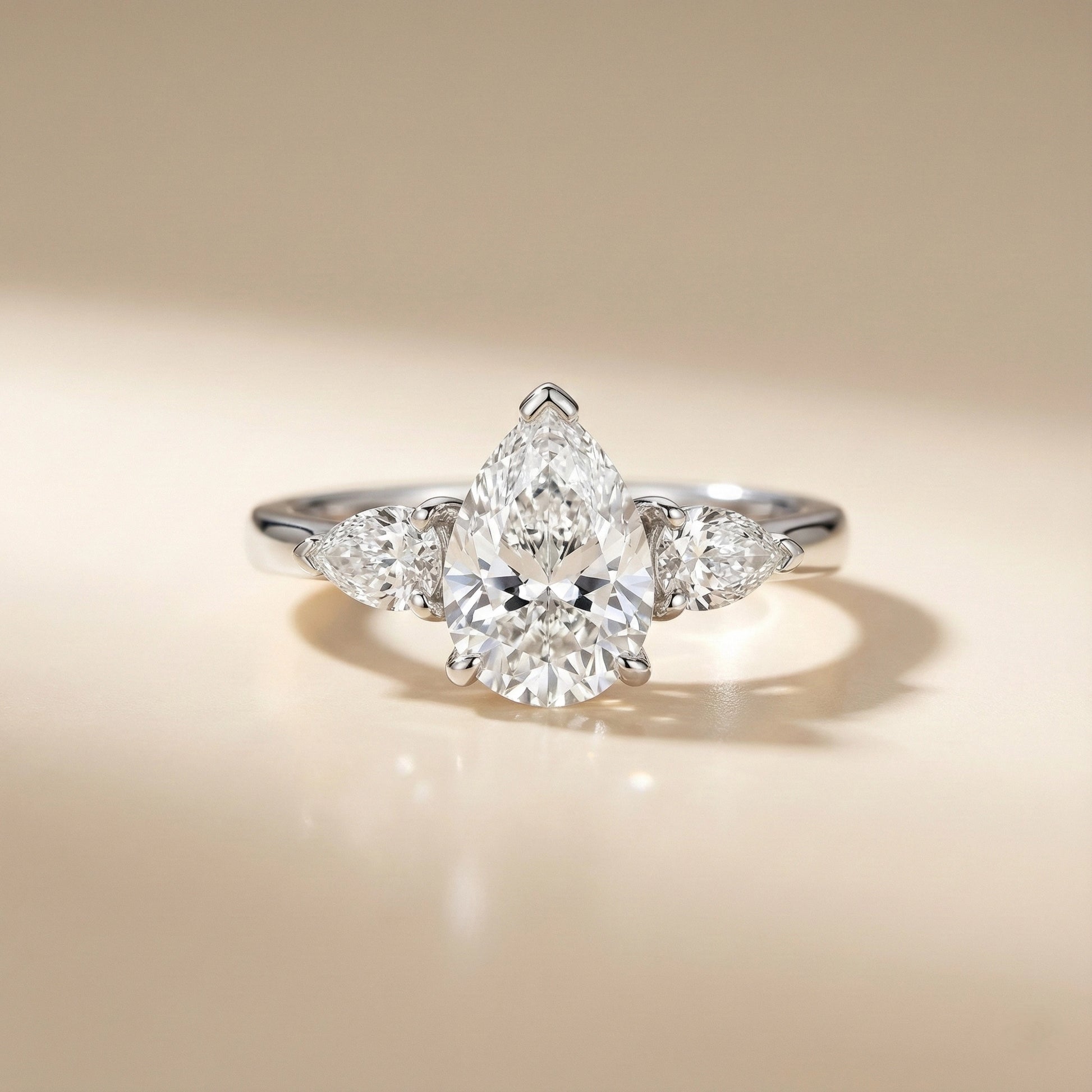 Diamond ring with a pear-shaped center stone on a beige background