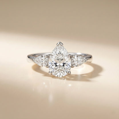 Diamond ring with a pear-shaped center stone on a beige background