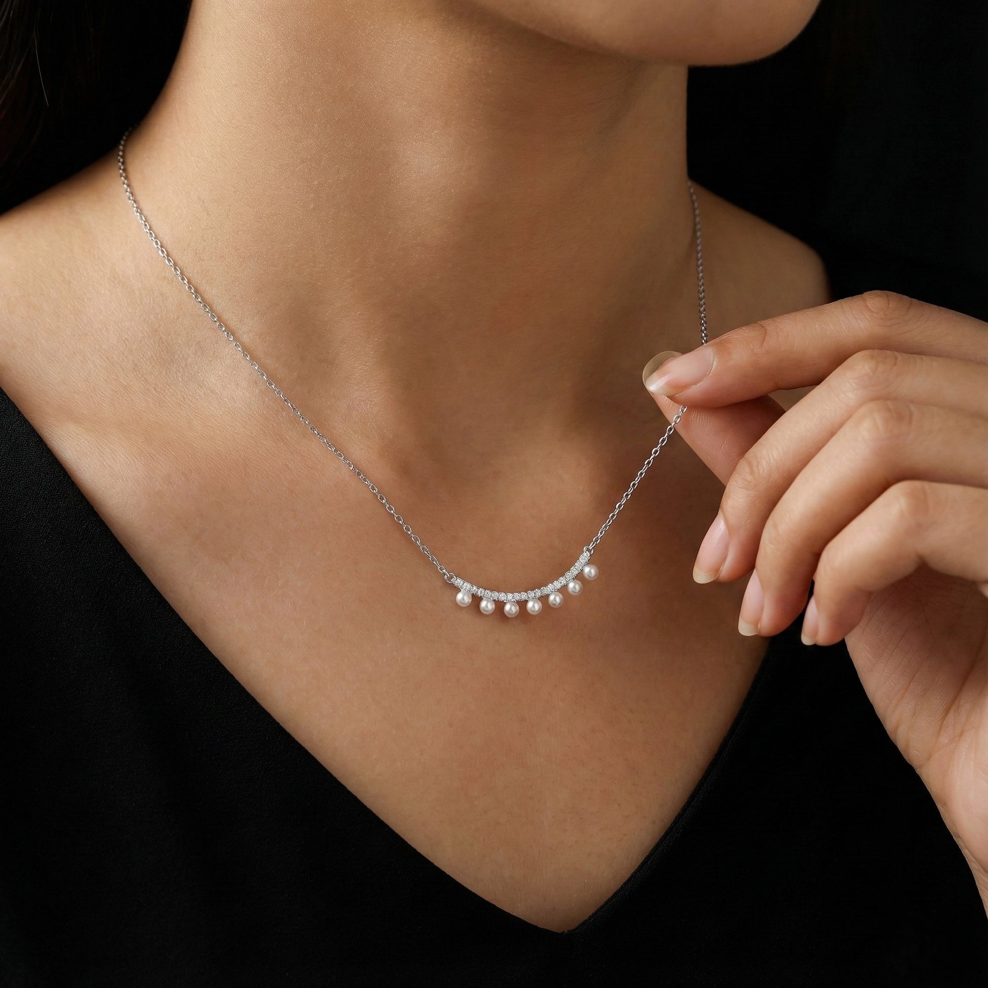Pearl necklace being worn and adjusted by a person against a black background